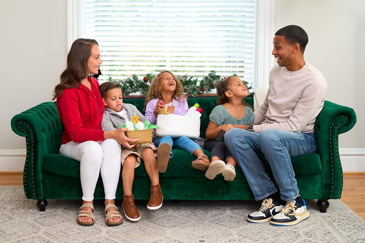 Family sitting on a green couch exchanging holiday gifts